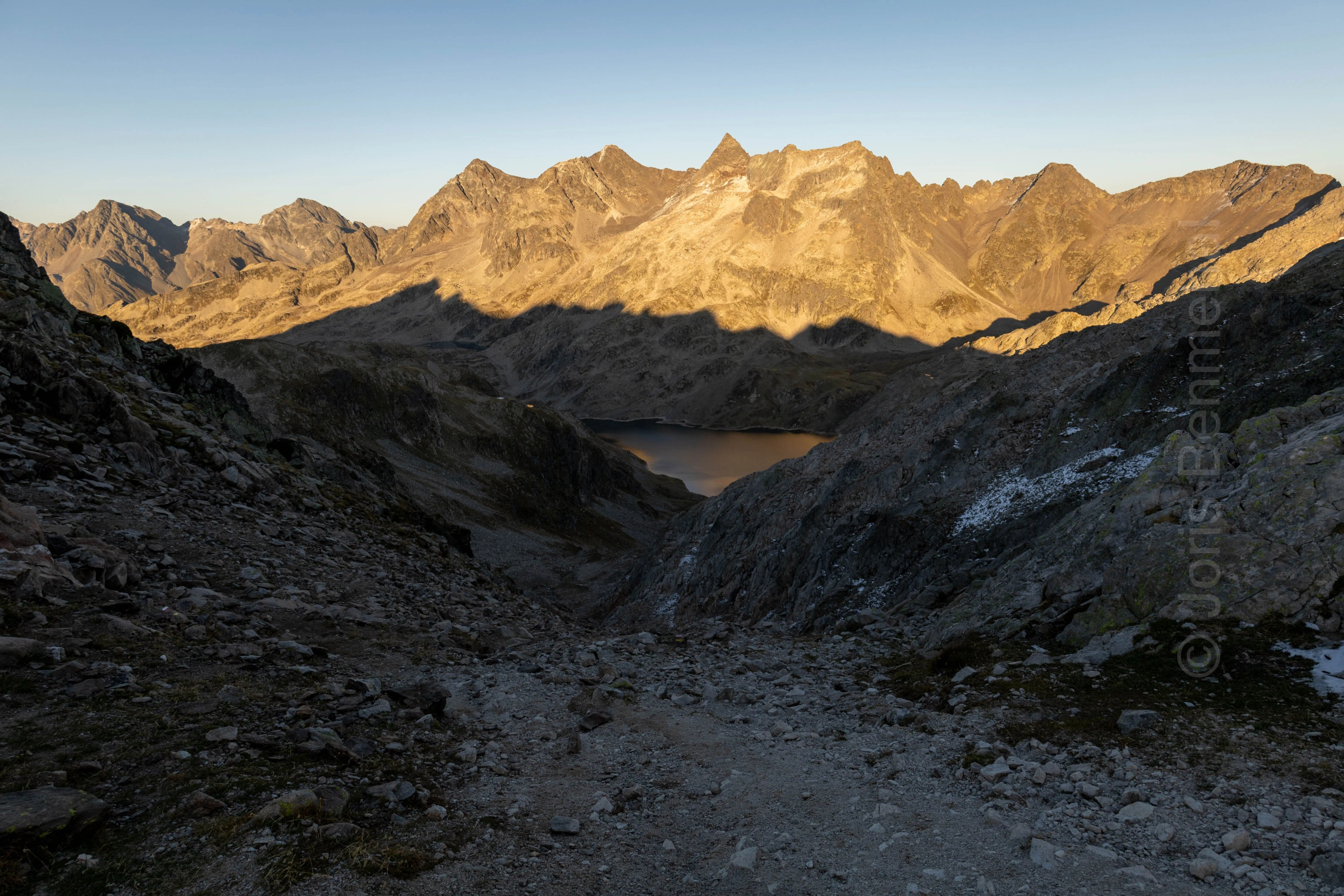 Vue du soir depuis le col de la Vache sur le GRP des 7 Laux, avec le lac du Cos encadré par des crêtes montagneuses et des éboulis.