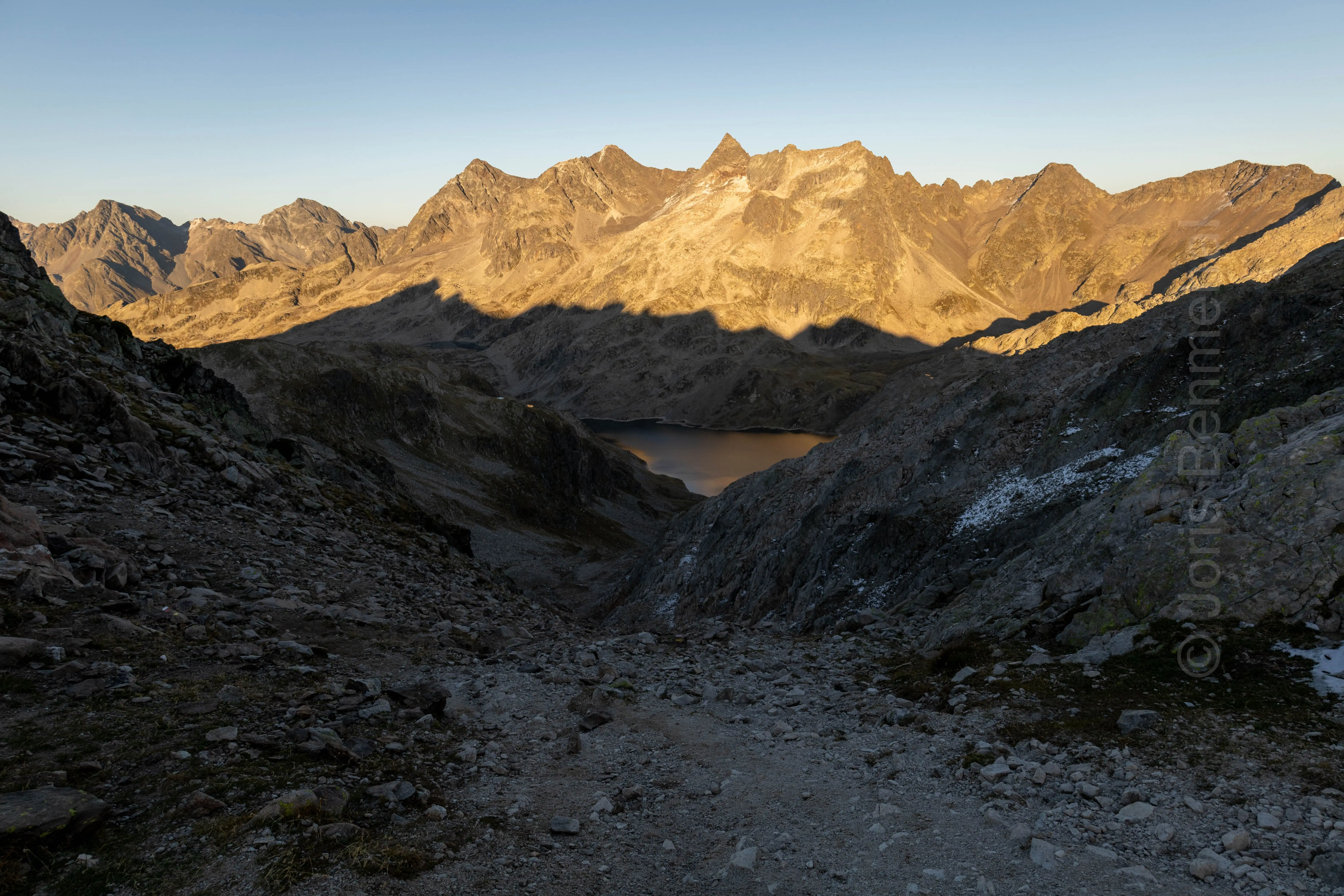 Vue du soir depuis le col de la Vache sur le GRP des 7 Laux, avec le lac du Cos encadré par des crêtes montagneuses et des éboulis.