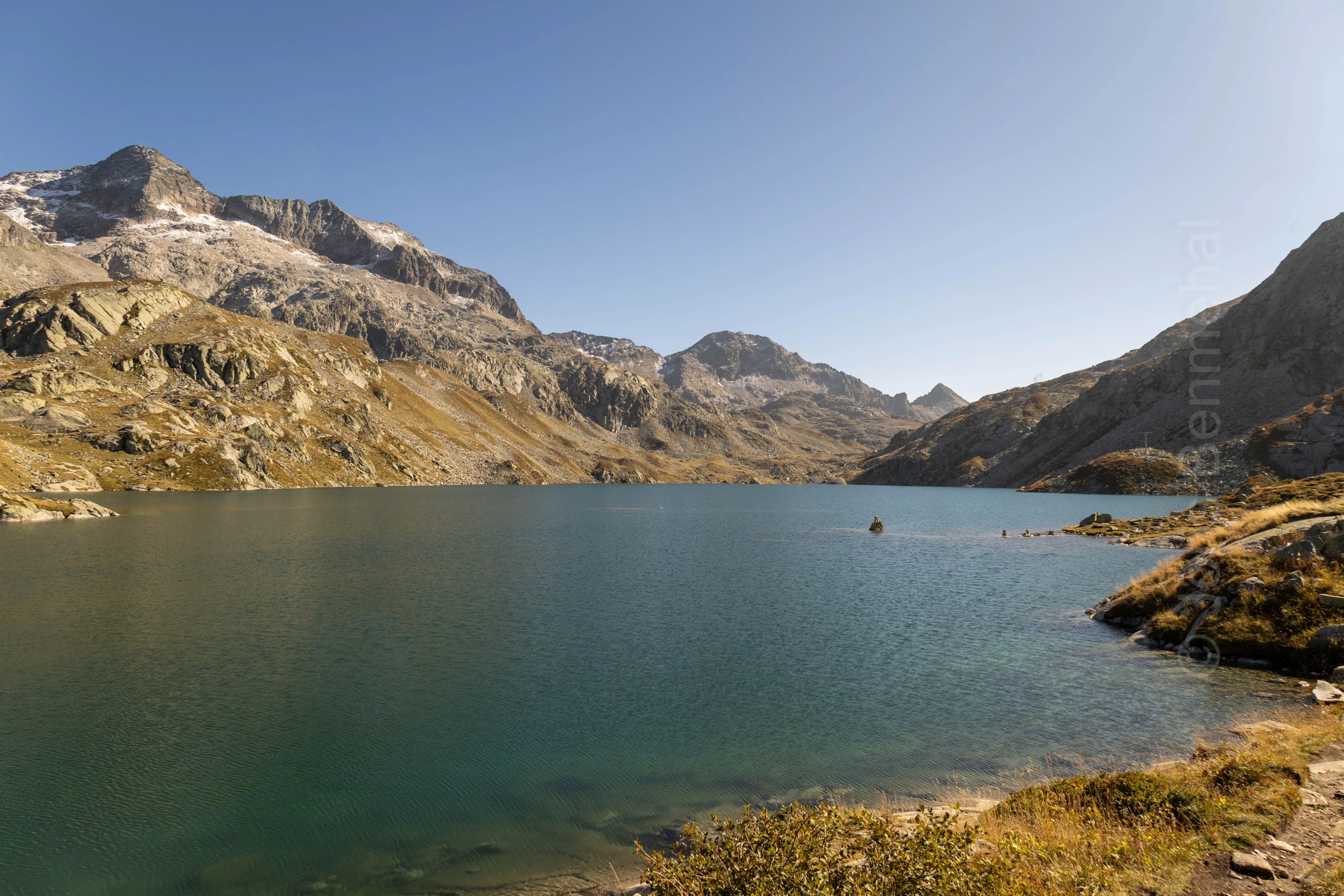 Lac de Cottepens serein bordé de montagnes rocheuses avec traces de neige, sur le parcours du GRP près du refuge des 7 Laux.