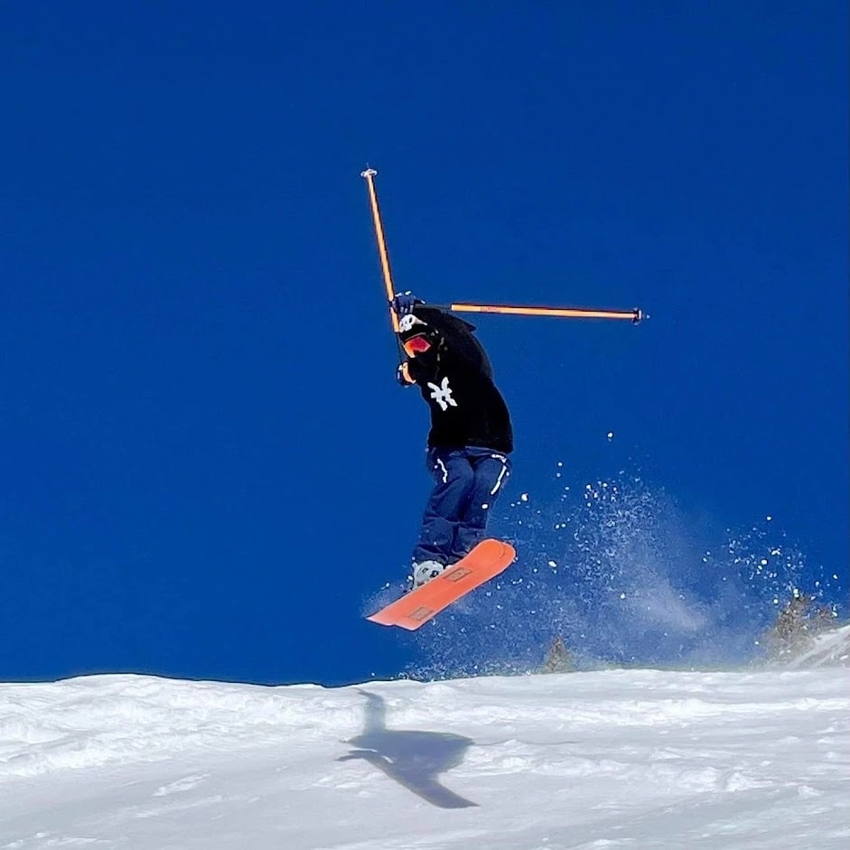 Benmehal Joris dans les airs en ski avec une trainée de poudreuse derrière lui avec les skis en parallèle