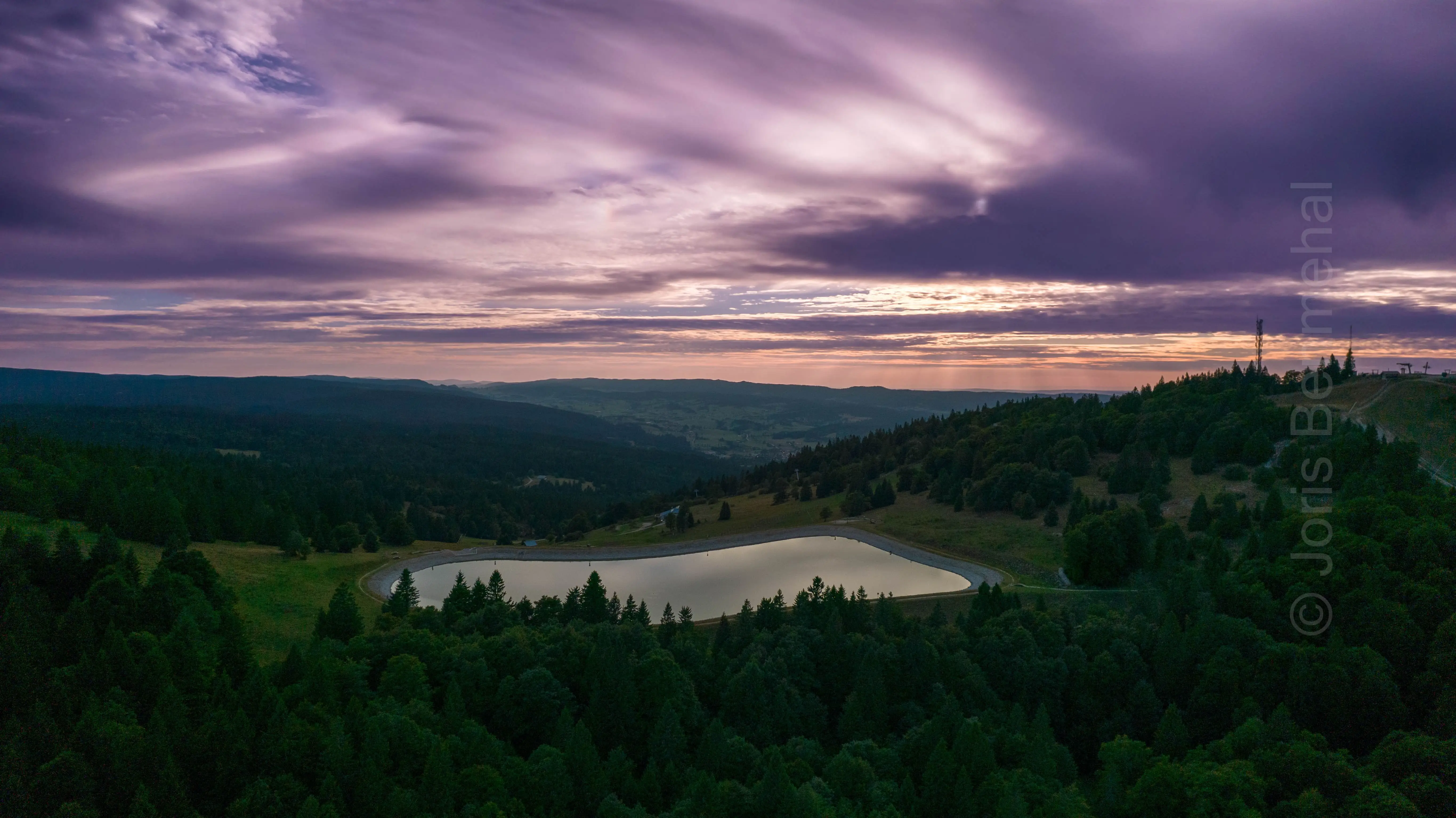 Lac artificiel du Morond capturé du ciel au coucher du soleil, ciel partagé entre violet et rouge.